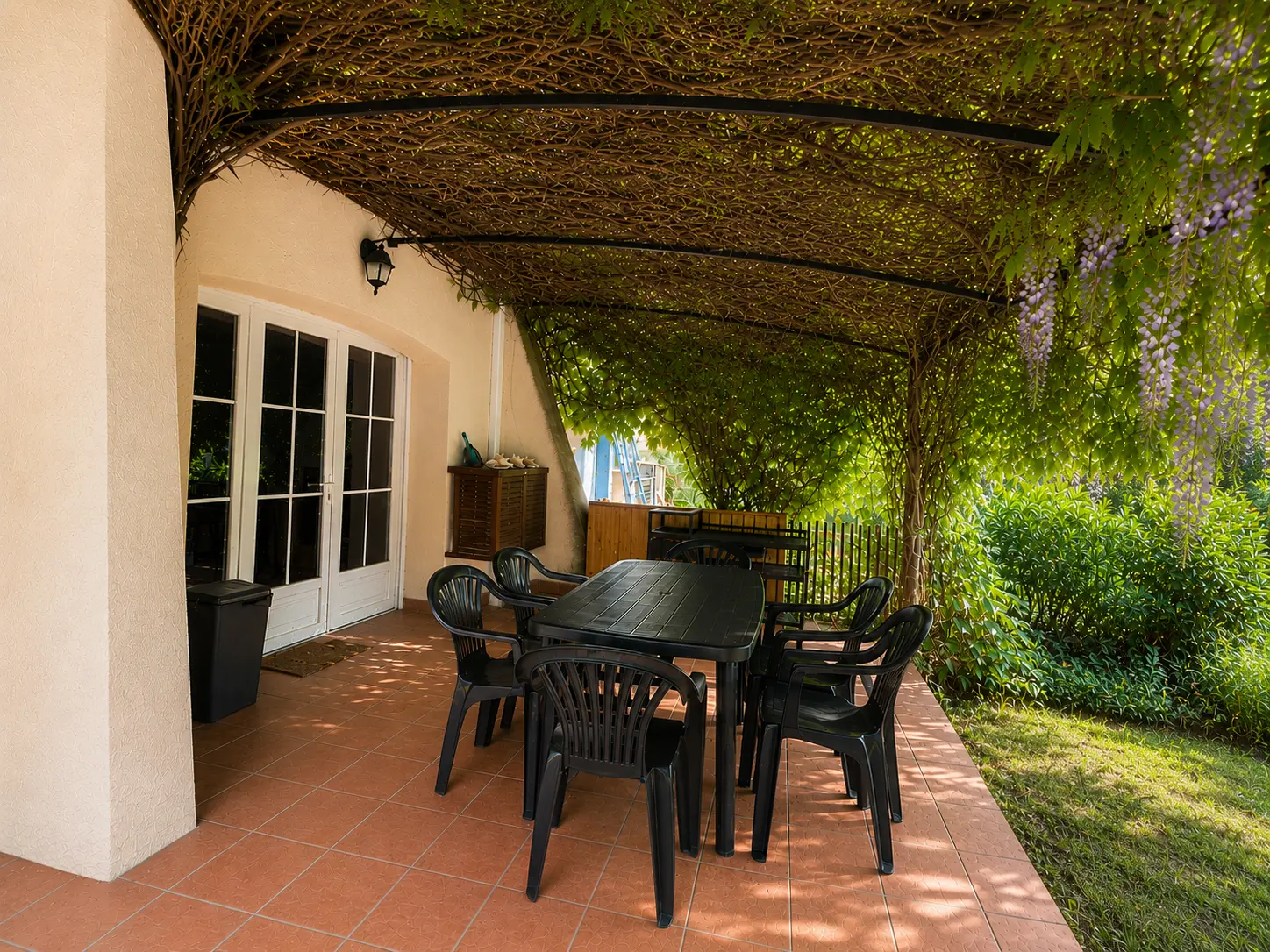 Terrasse ombragée du gîte sous une glycine, avec table et chaises